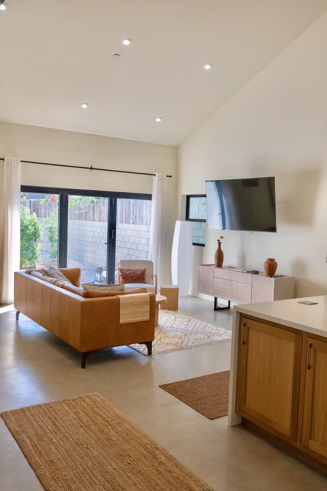 Living room in the front house with vaulted ceiling, leather sofa, oak cabinetry and doors opening to the patio.